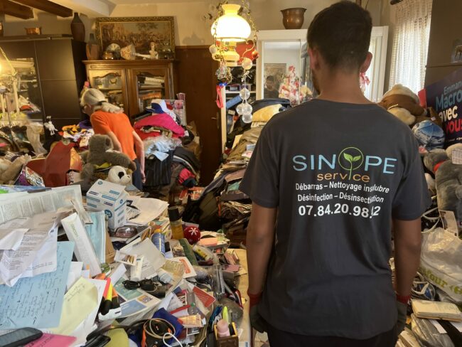 Salarié de Sinope Service vu de dos lors d’une intervention dans une pièce très encombrée.