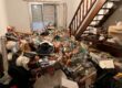 Pièce de vie avec une accumulation d’objets autour du mobilier et d’un escalier en bois.