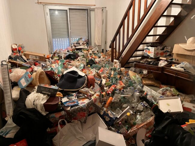 Pièce de vie avec une accumulation d’objets autour du mobilier et d’un escalier en bois.